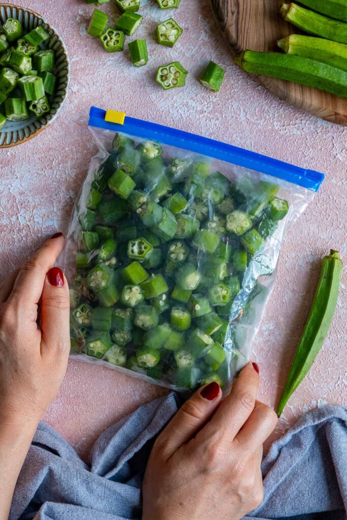 Hands holding a freezer bag filled with sliced okra.